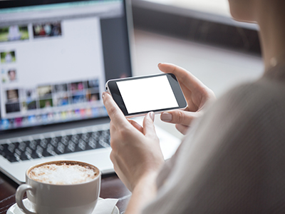 Female hands holding smartphone with empty blank screen for copy space in coffee shop. Rear view. Woman sitting with cup of coffee and using electronic devices. Close-up
