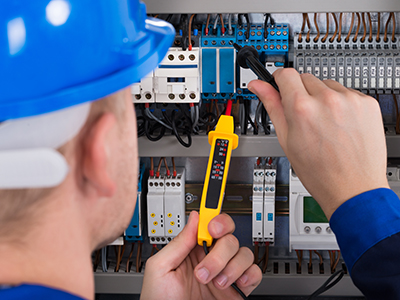 Electrician investigating a fault in a mechanical services switch board with a volt meter